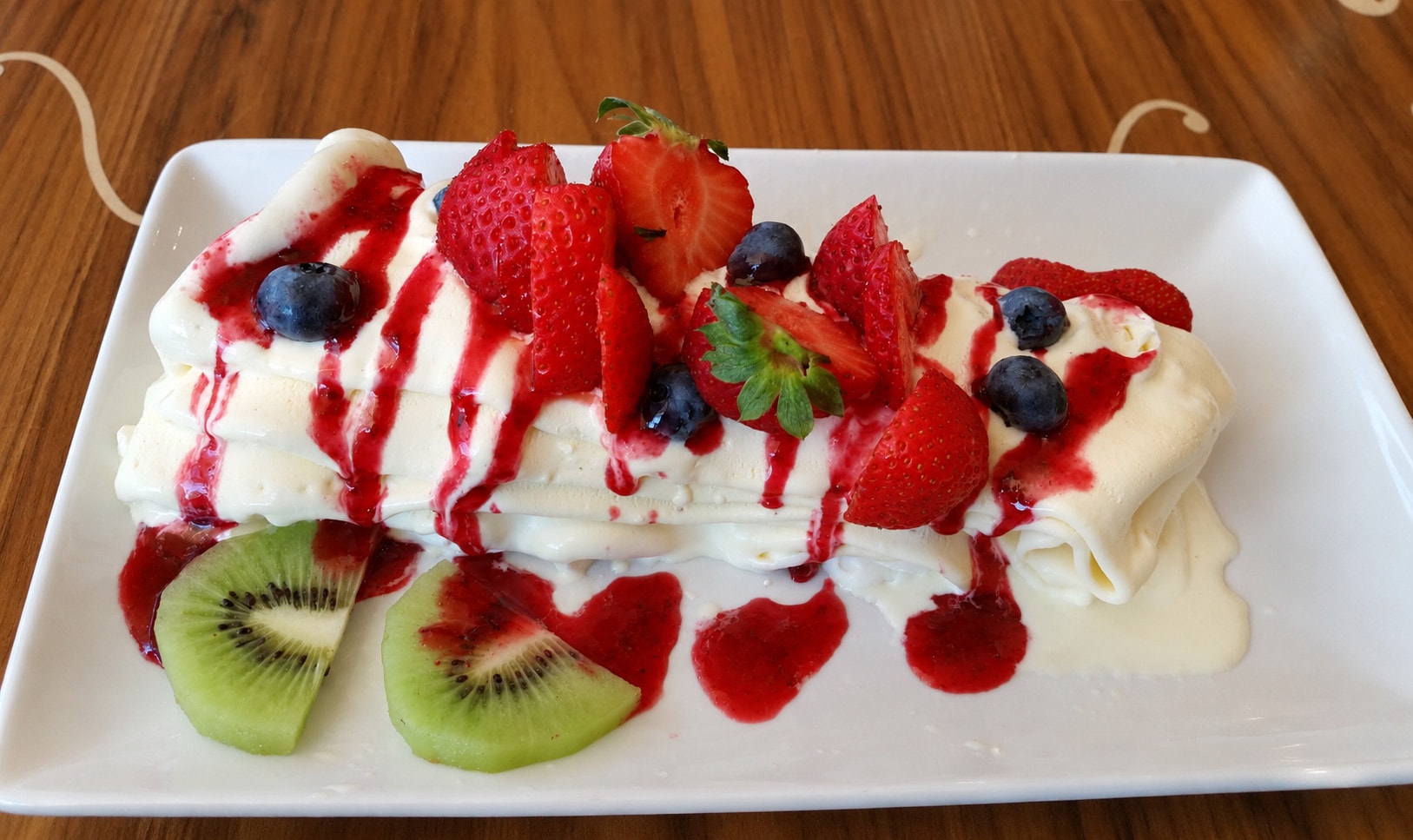 A rolled crêpe with cream, strawberries, blueberries, kiwi and raspberry sauce