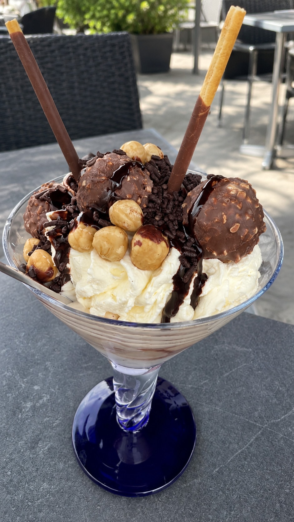 A nut sundae with hazelnuts, chocolate pralines, chocolate sauce and two wafer rolls in a blue-stemmed glass
