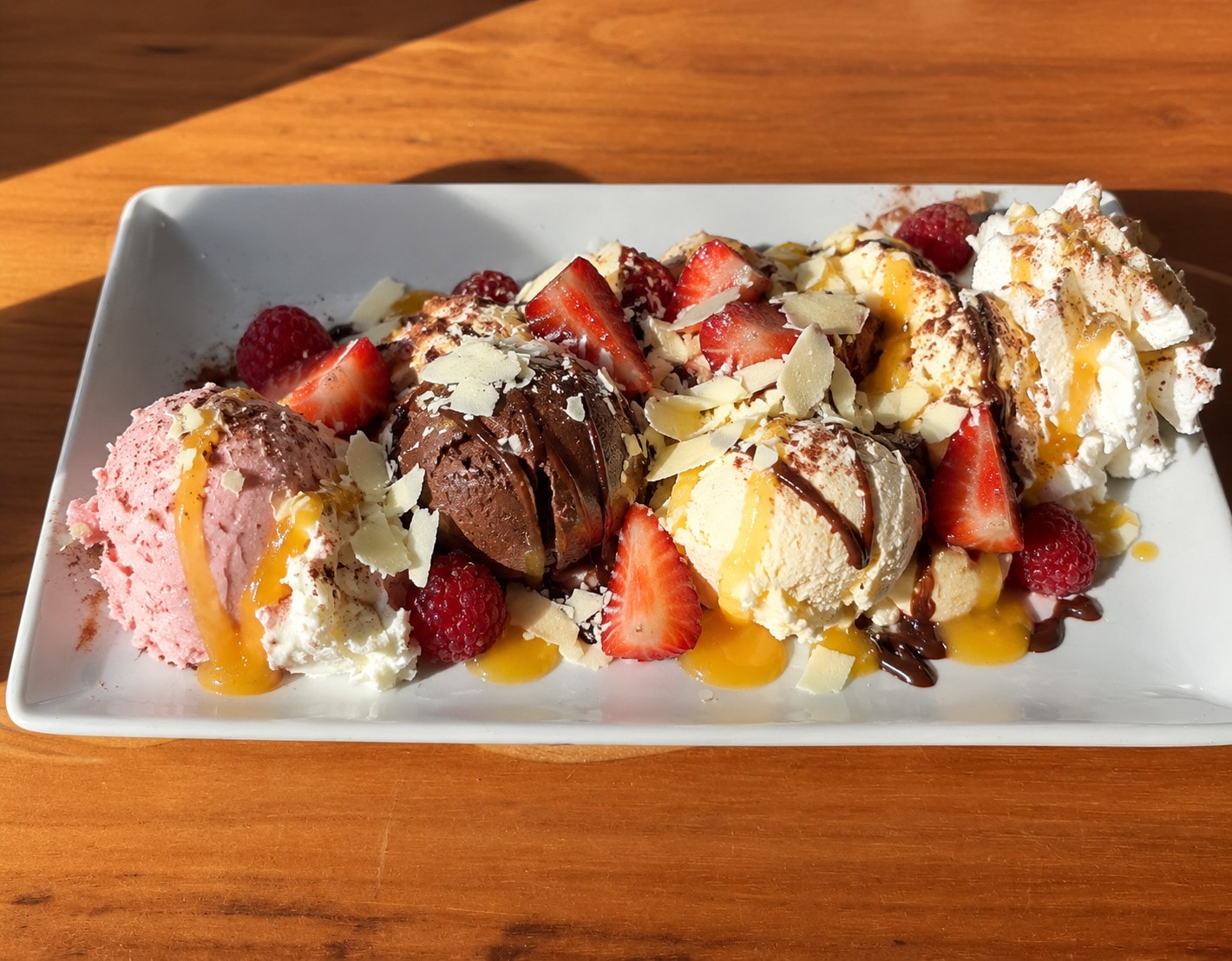 A plate of strawberry, chocolate and vanilla scoops with fresh berries, mango sauce and white chocolate curls
