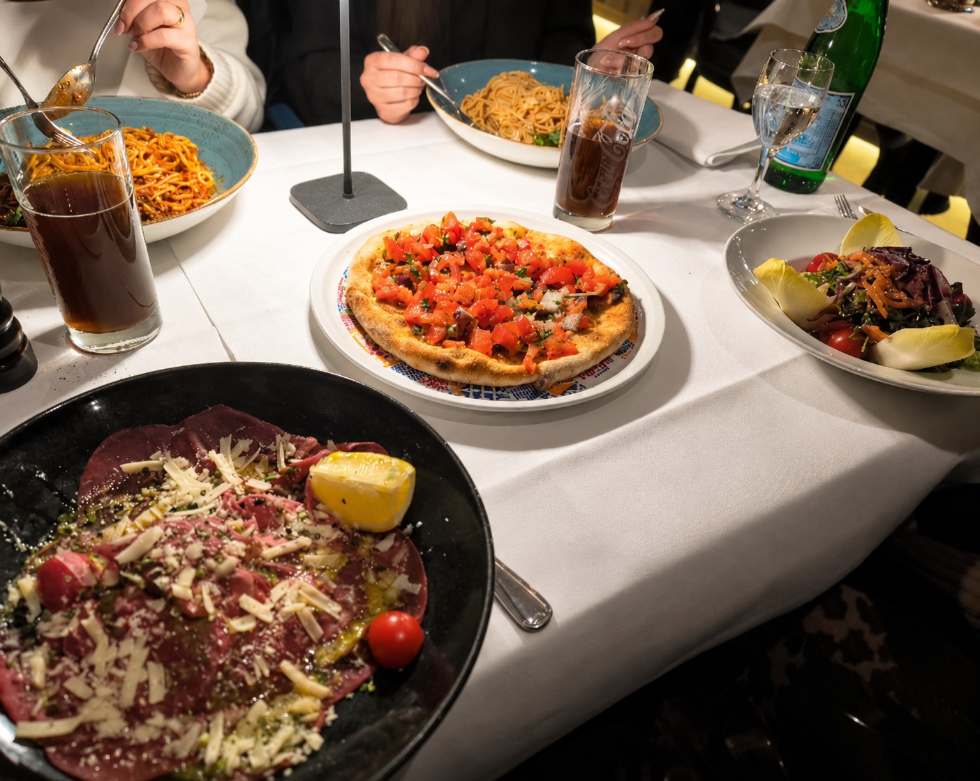 A full table of carpaccio, pizza bread, salad and pasta to share
