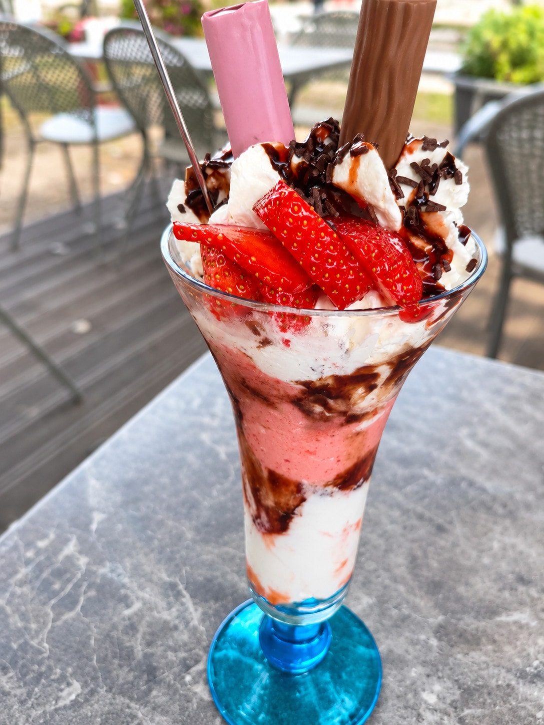 A strawberry sundae with fresh strawberries, cream, chocolate sauce and wafer rolls in a blue glass on the terrace