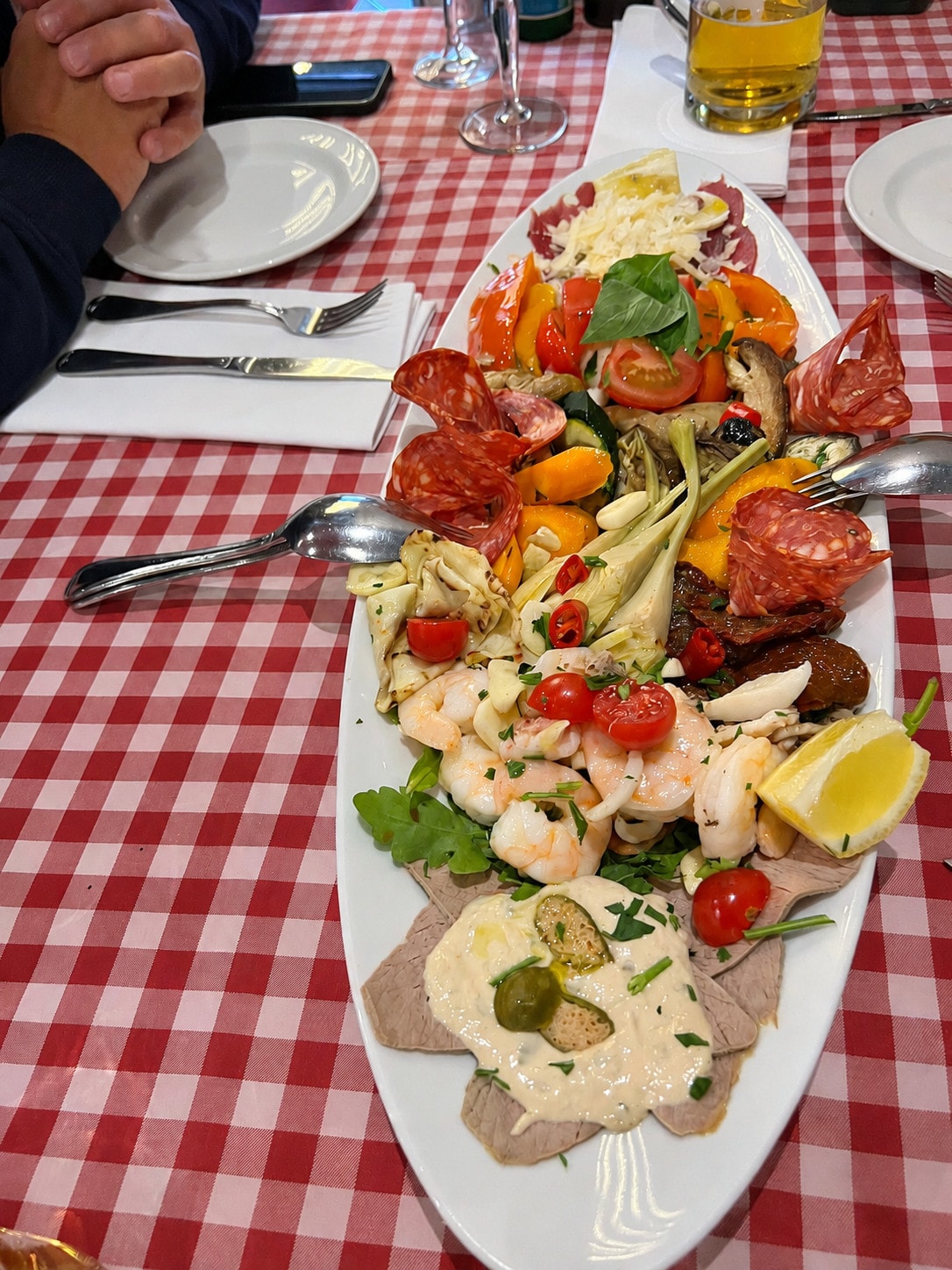 Large antipasti platter with prawns, salami, grilled vegetables and vitello tonnato on a checked tablecloth