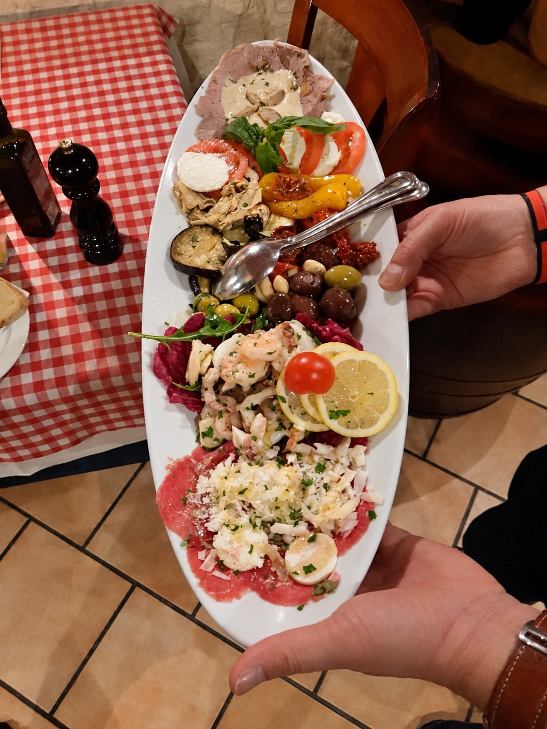 An antipasti platter with carpaccio, caprese and seafood being brought to the table