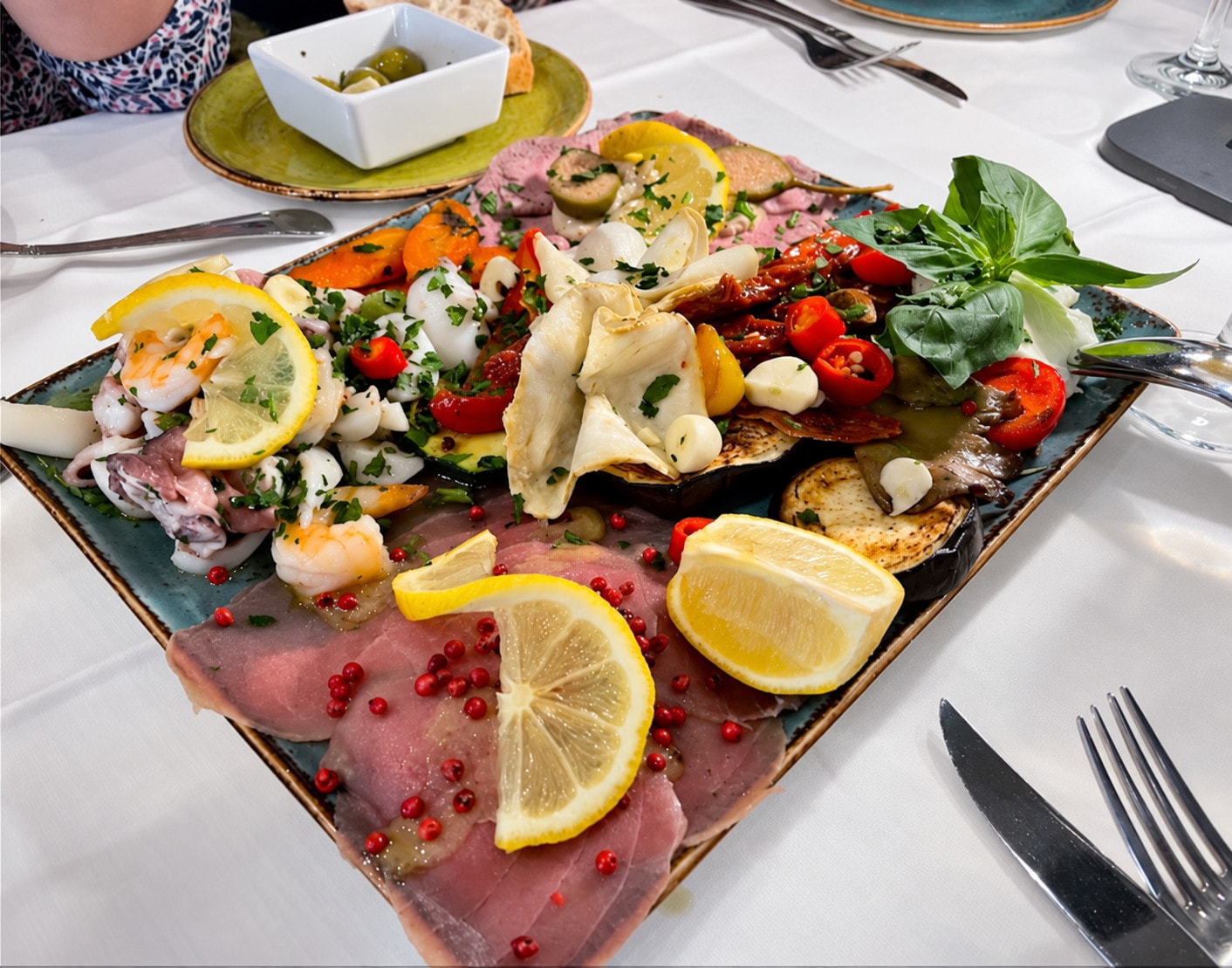 Antipasti on a square platter: vitello tonnato with pink pepper, seafood and grilled vegetables
