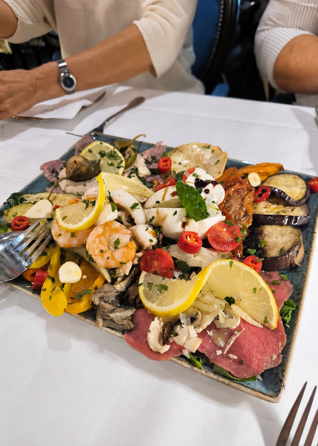 A square platter of seafood, carpaccio, lemons and marinated vegetables