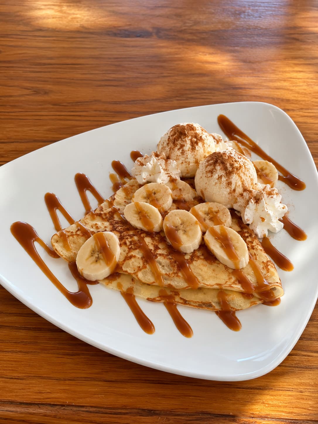 A crêpe with banana slices, two scoops of gelato, cream and caramel sauce
