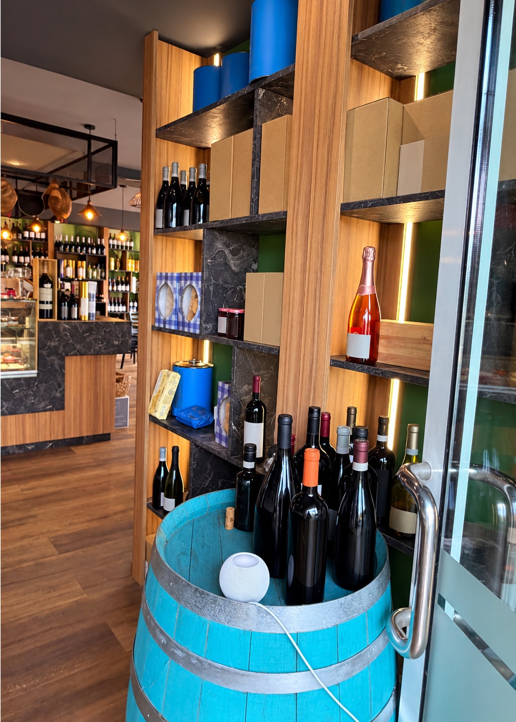 A turquoise barrel full of wine bottles in front of the Salumeria wine shelves