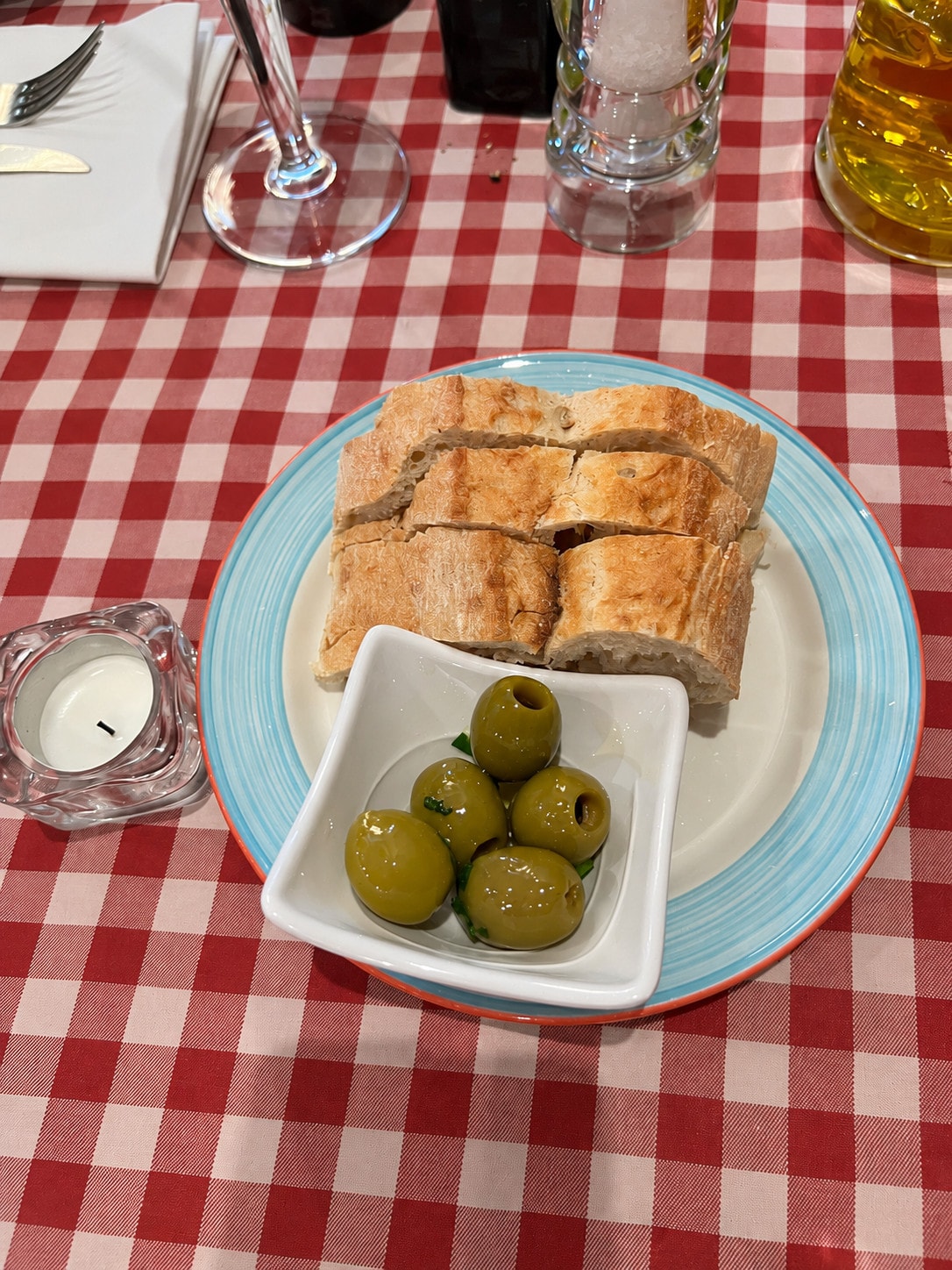 Homemade bread and green olives on a plate beside a tealight