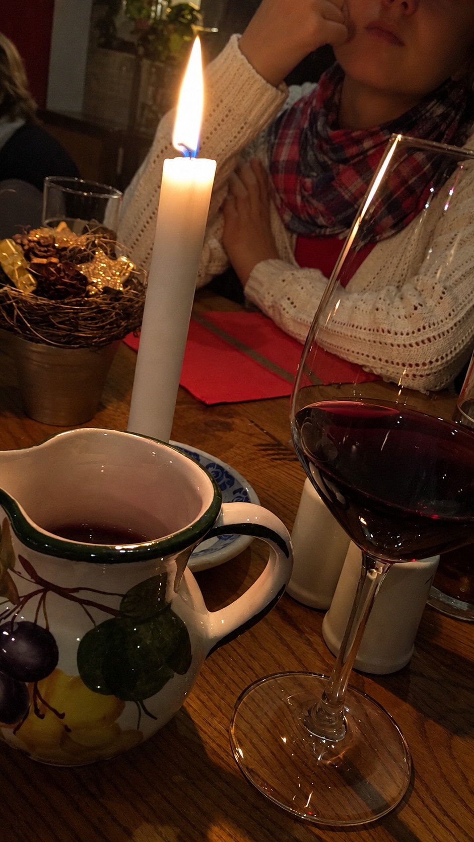 A lit candle, a wine jug and a glass of red wine on the table in the evening