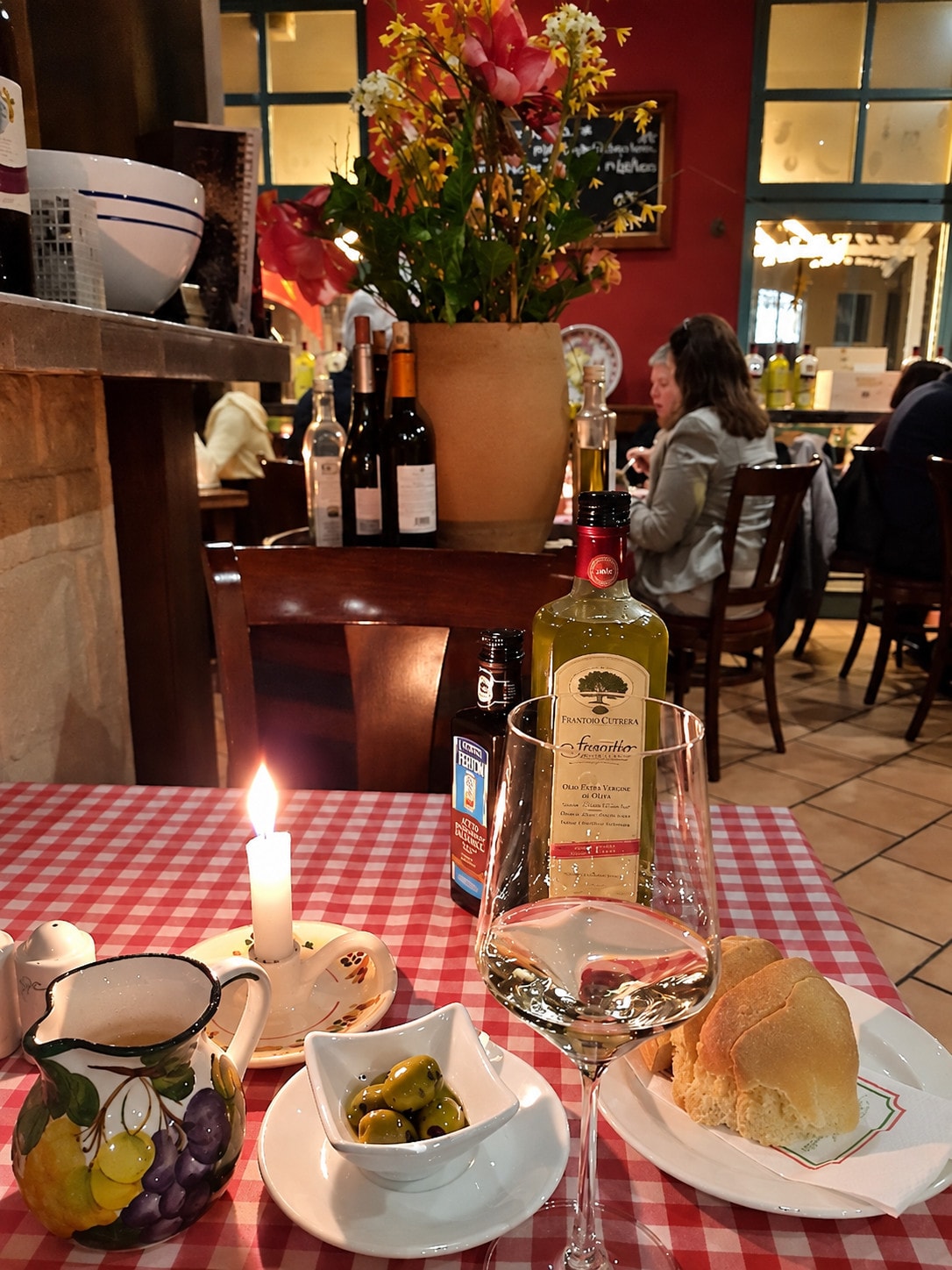 A candlelit table set with white wine, olive oil, olives and bread