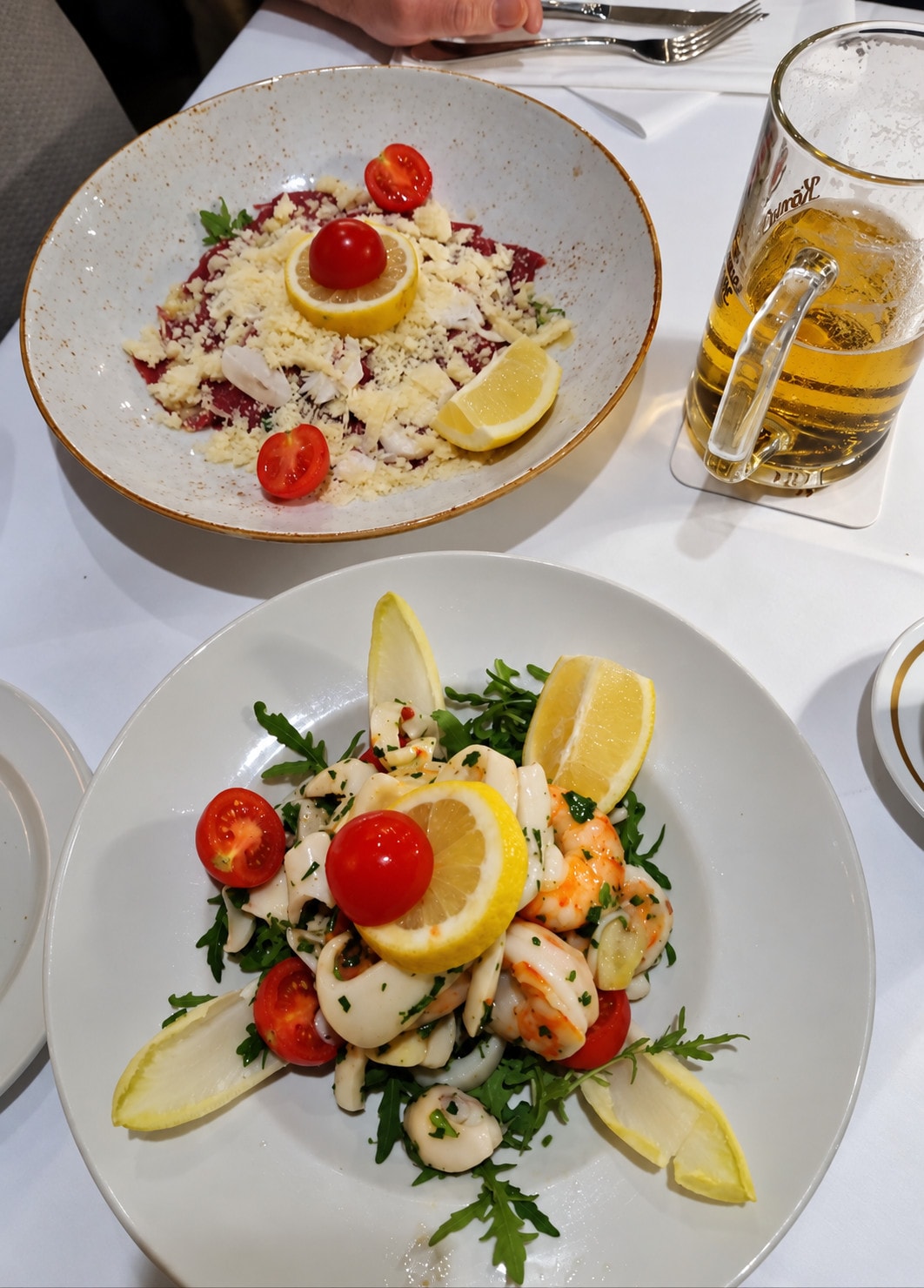 Two plates: carpaccio with parmesan and a seafood salad with lemon and rocket
