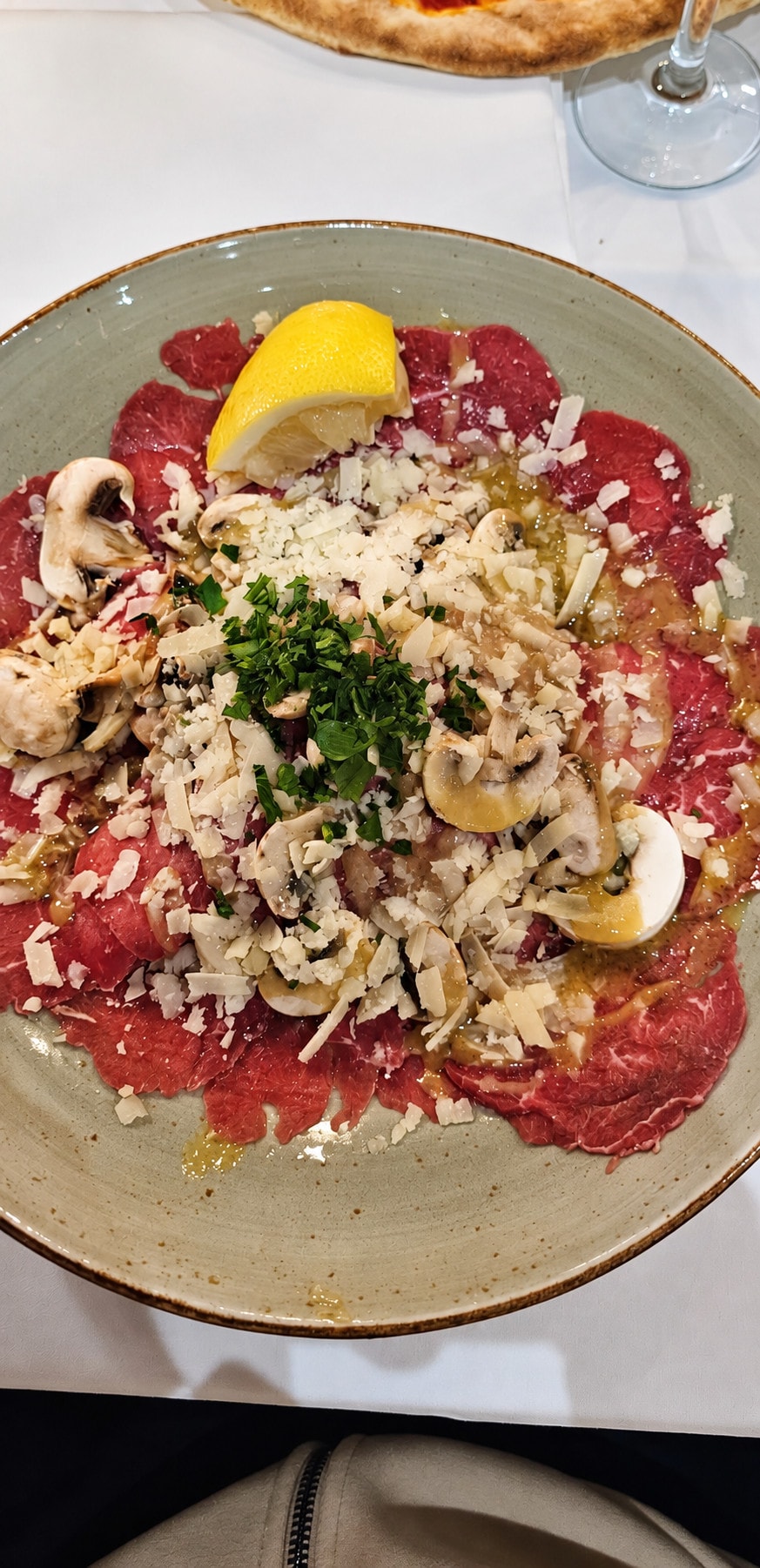Carpaccio with mushrooms, parmesan, parsley and lemon on a stoneware plate