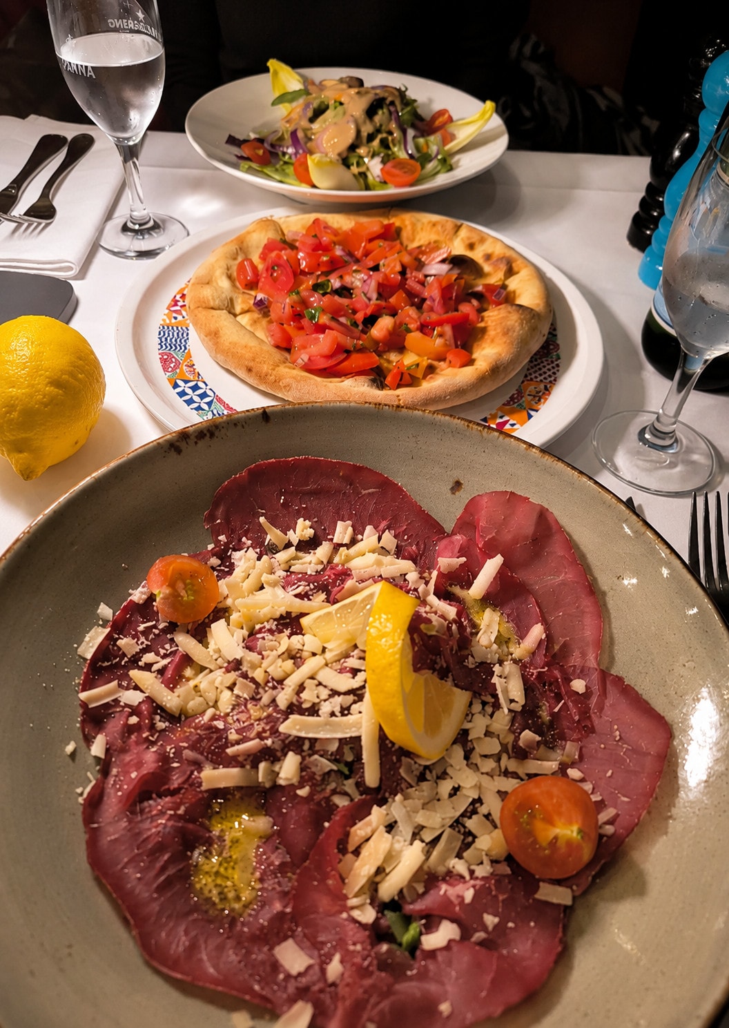 Carpaccio with parmesan in front, pizza bread and a salad behind