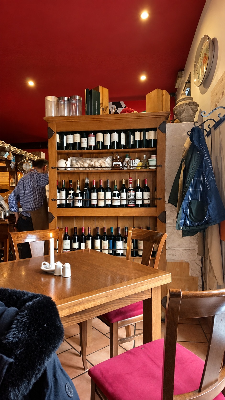 A cosy corner of the dining room with a wooden table, a candle and a shelf of wine