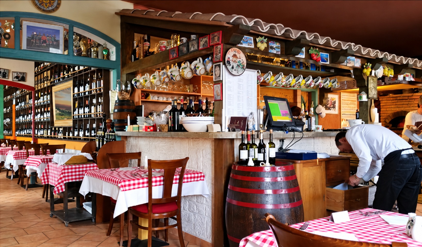 The dining room with red-and-white checked tables, a wine barrel and the bar behind