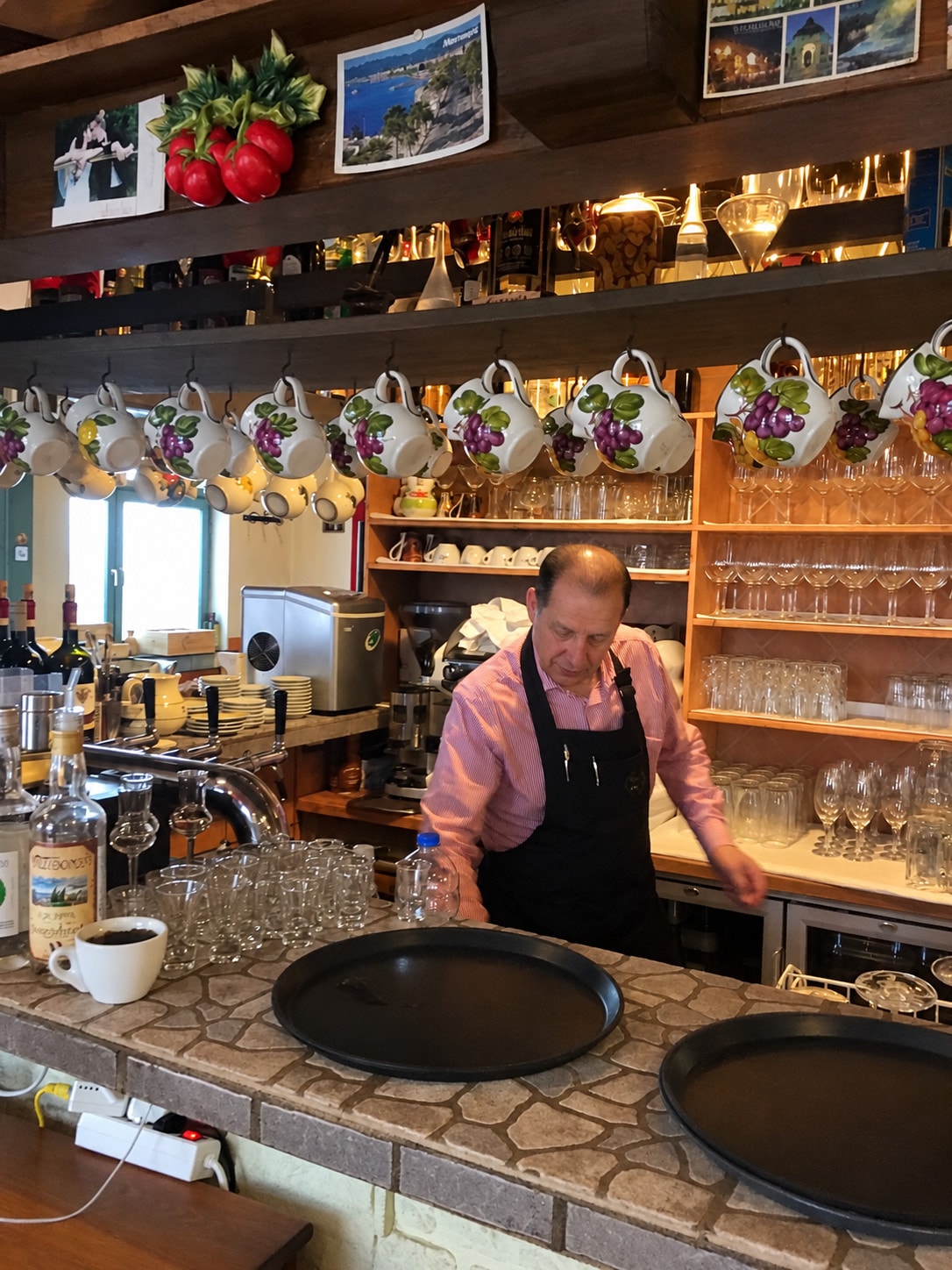 The host behind the bar beneath rows of cups, glasses and keepsakes