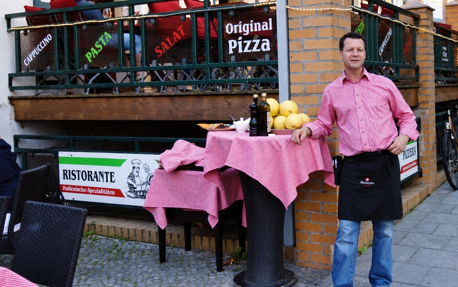 The host leaning, smiling, against a dressed table in front of the terrace