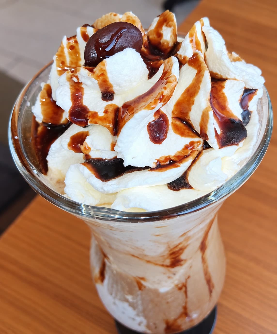 Iced coffee in a tall glass with whipped cream, chocolate sauce and a chocolate bean