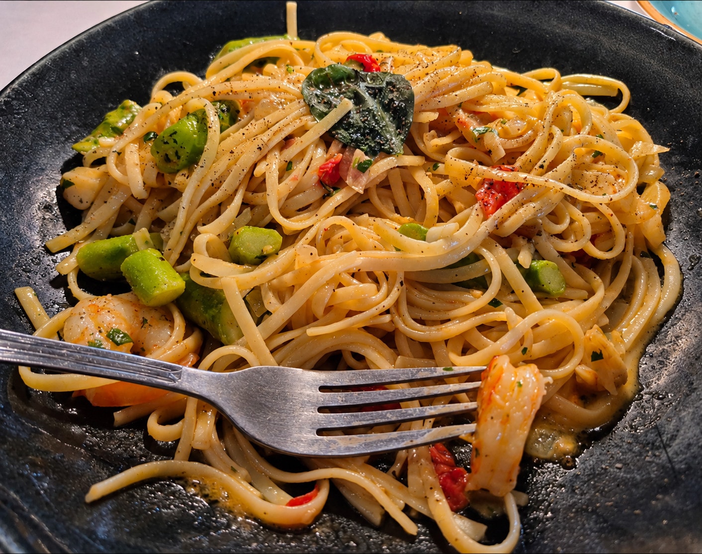 Linguine with prawns, green asparagus and tomato on a dark plate