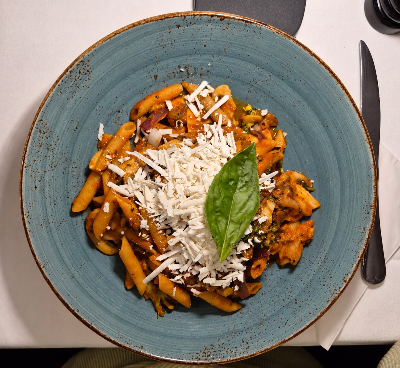 Penne with tomato sauce, ricotta and basil from above on a blue plate