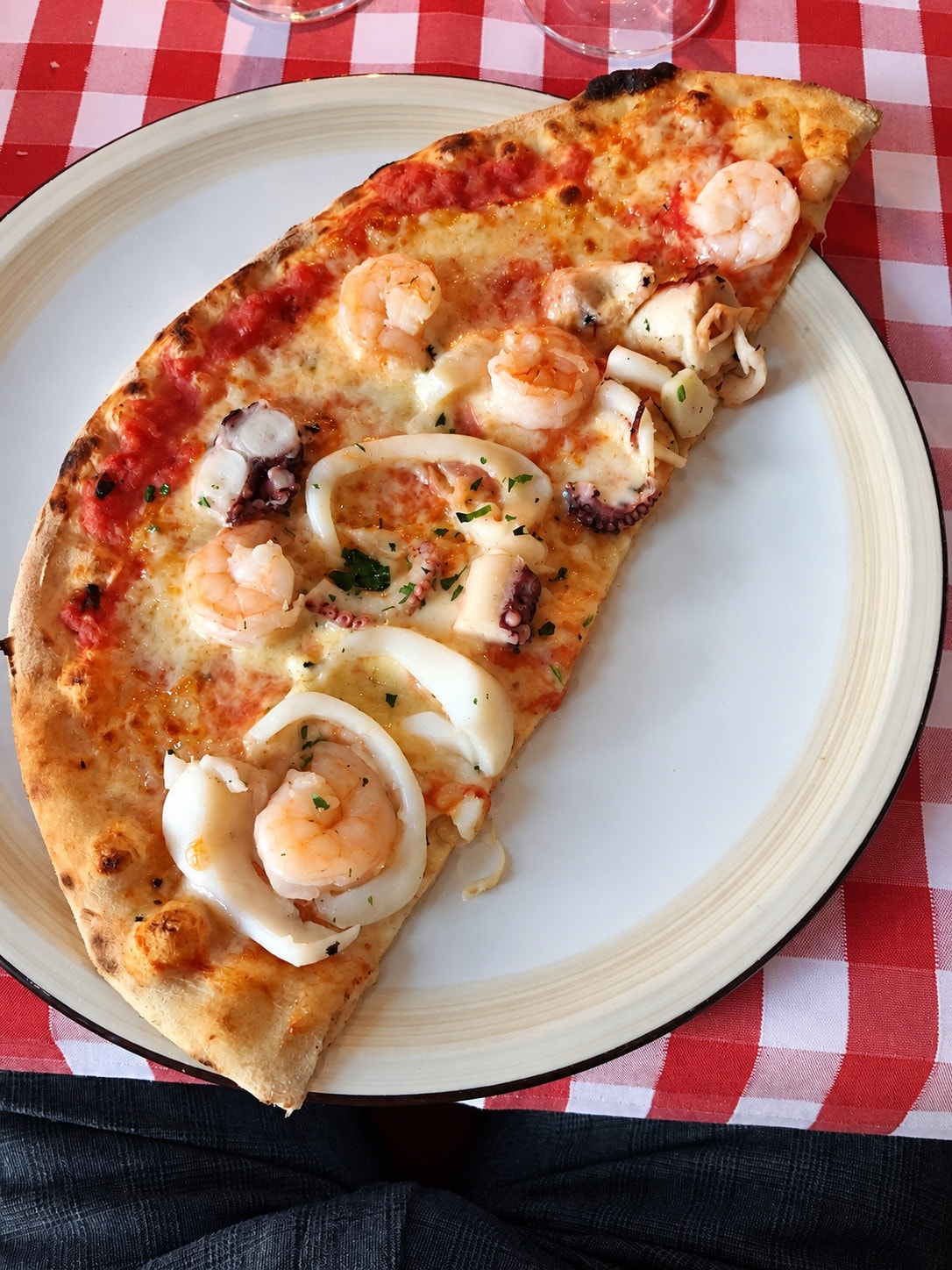 Pizza topped with prawns and squid rings on a plate over a red-and-white checked cloth