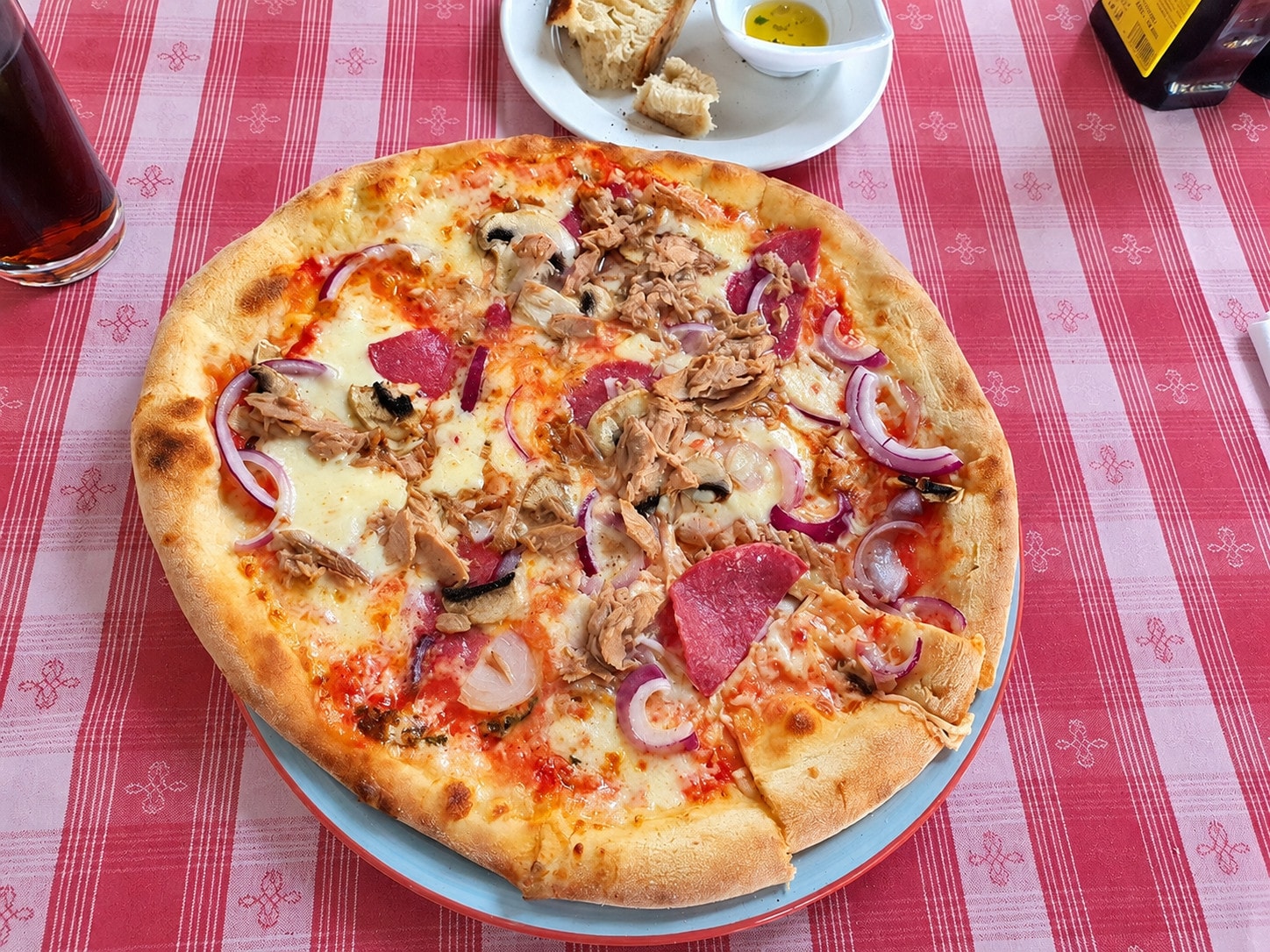 Pizza with tuna, salami, mushrooms and red onion, with bread and olive oil alongside