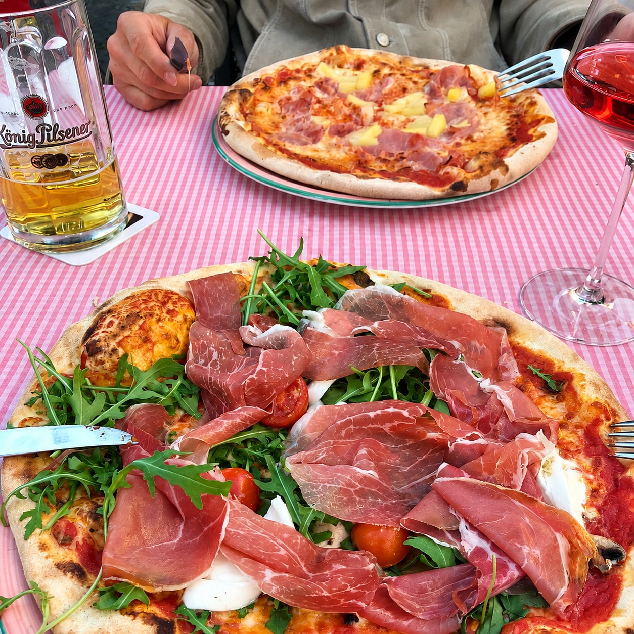 Pizza with Parma ham, rocket and cherry tomatoes, a pizza Hawaii and a beer behind it
