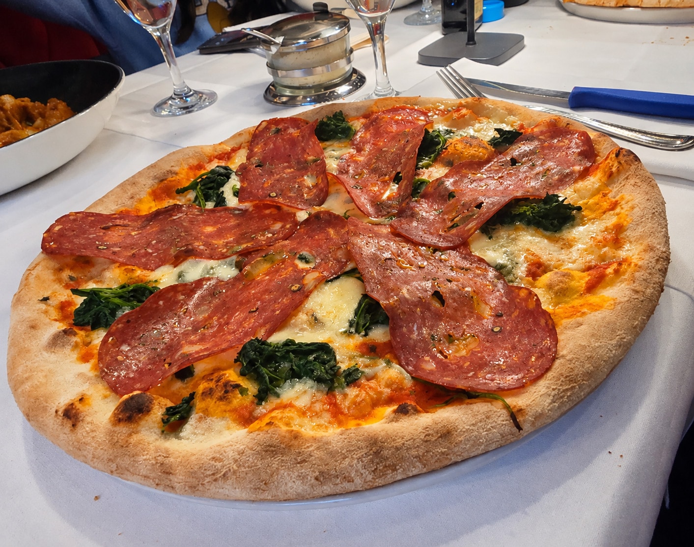 Pizza with spicy salami, spinach and gorgonzola on a white tablecloth