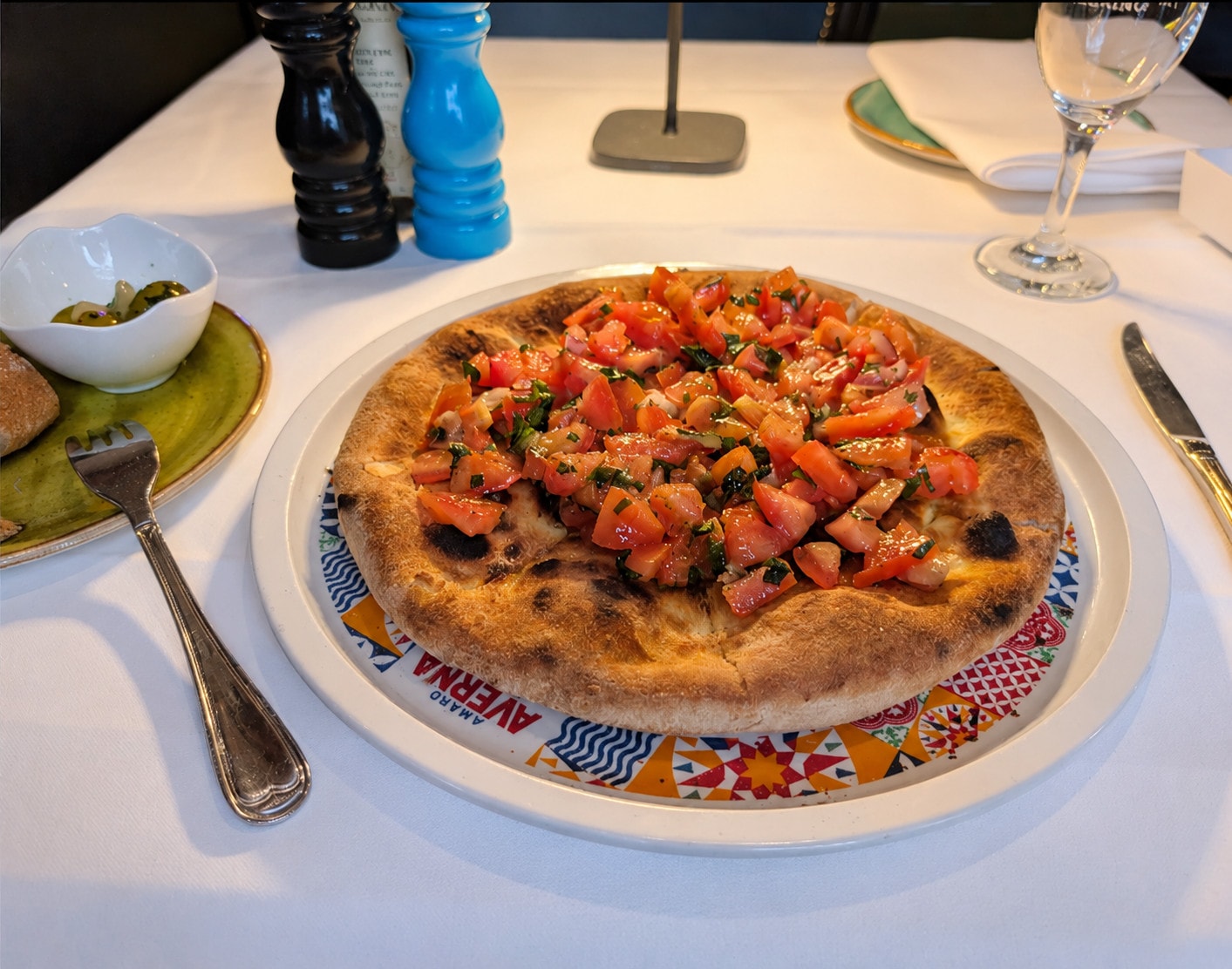 Oven-fresh pizza bread with diced tomato on a colourful plate, olives alongside