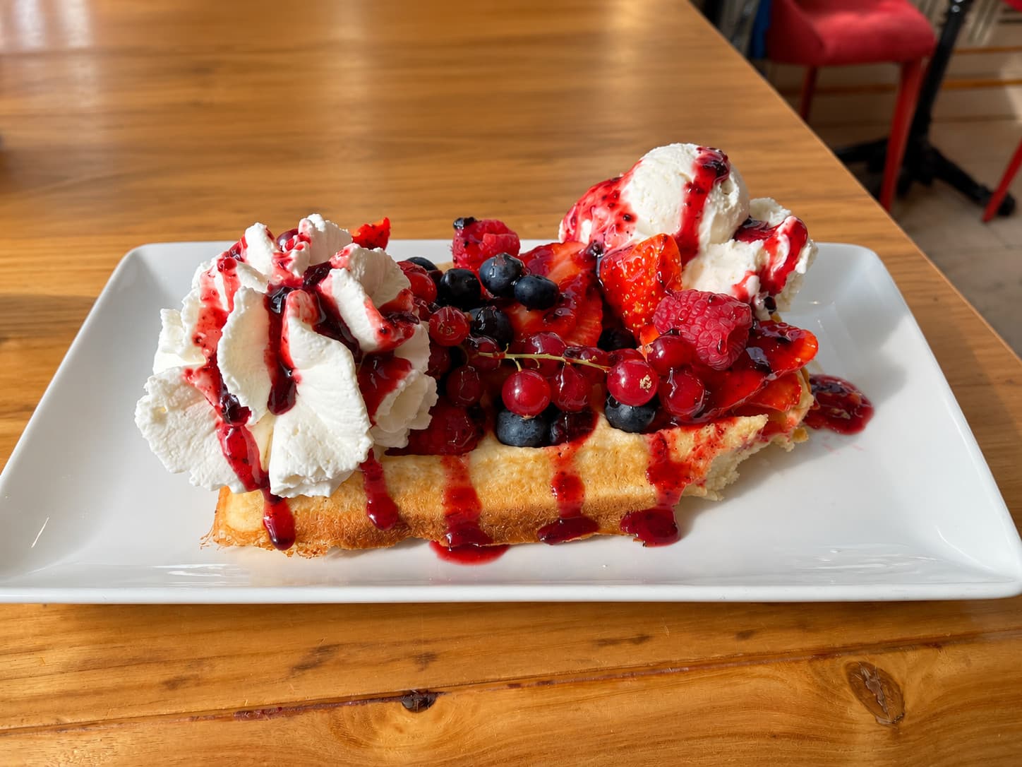 A waffle with cream, redcurrants, strawberries, blueberries and red berry sauce