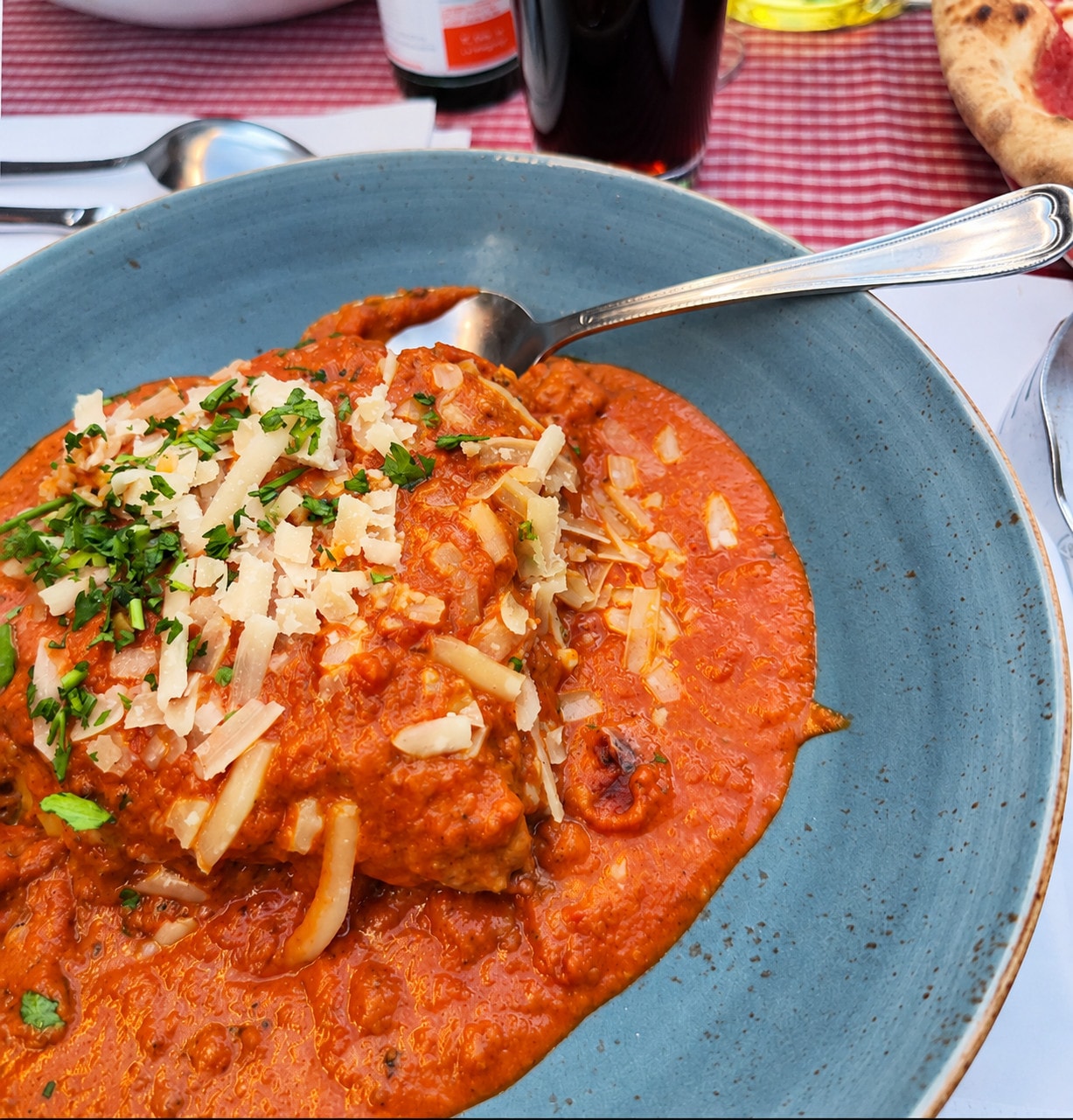 Scaloppina in tomato sauce with shaved parmesan and parsley on a blue plate