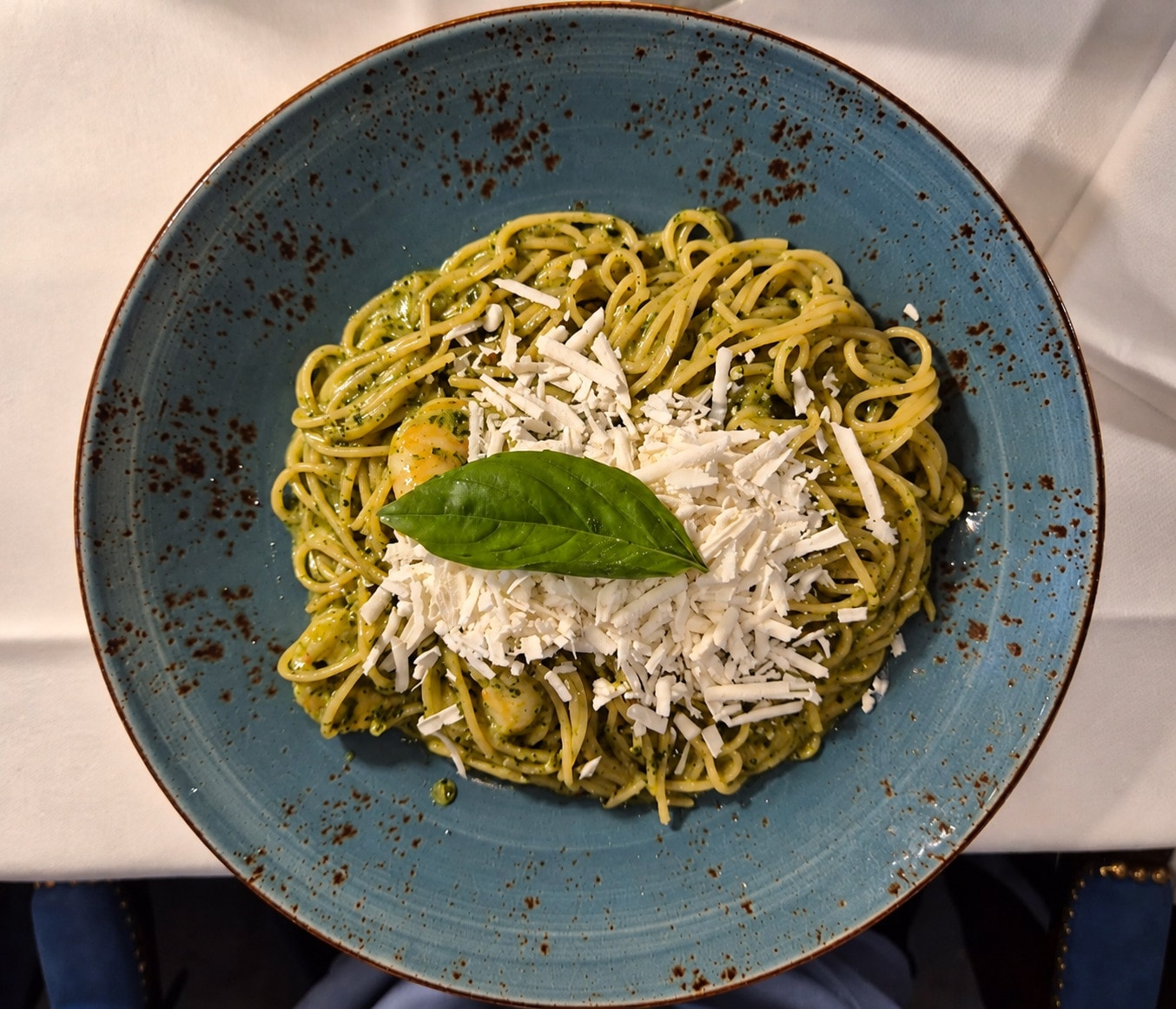 Spaghetti with pesto, grated cheese and basil on a blue plate