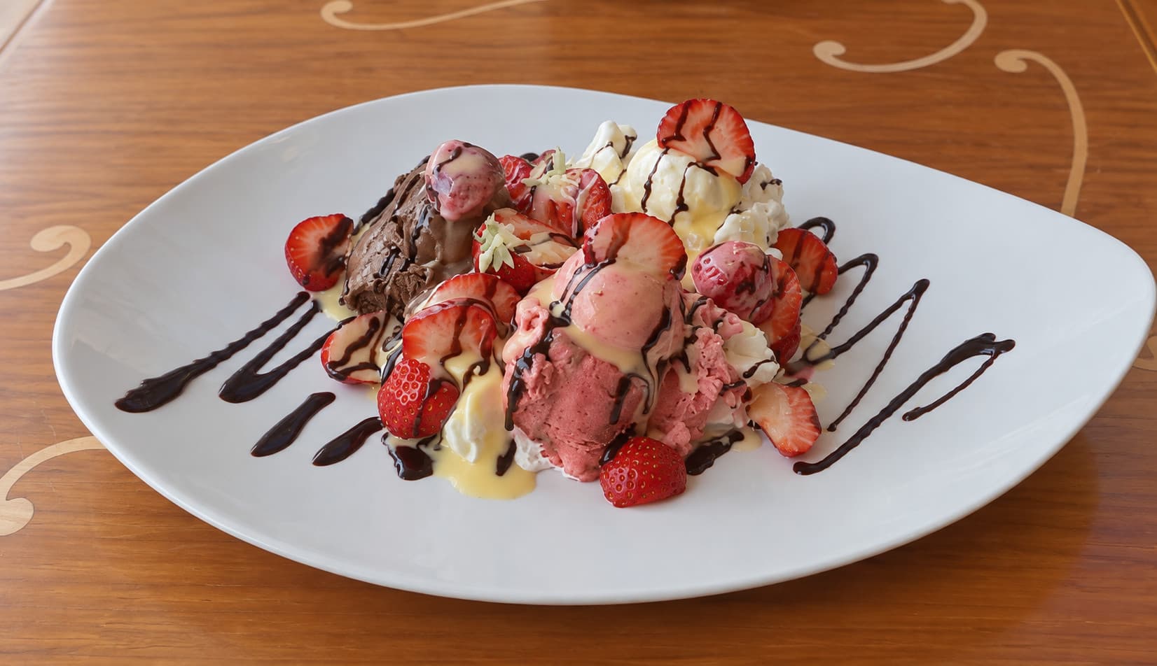 Strawberry and chocolate gelato with fresh strawberries, vanilla sauce and a chocolate drizzle on a plate