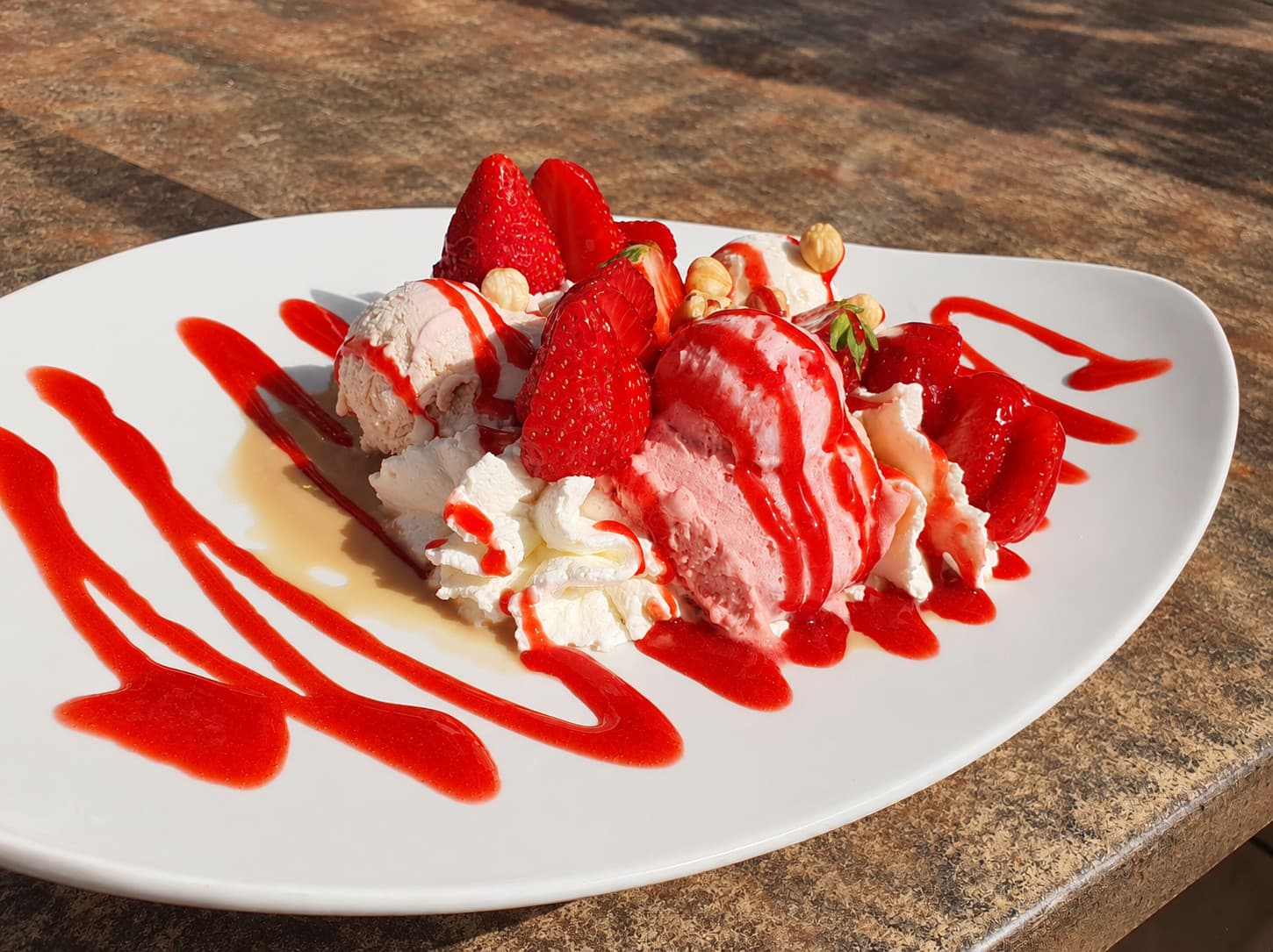 Strawberry gelato with fresh strawberries, cream, hazelnuts and strawberry sauce on a white plate