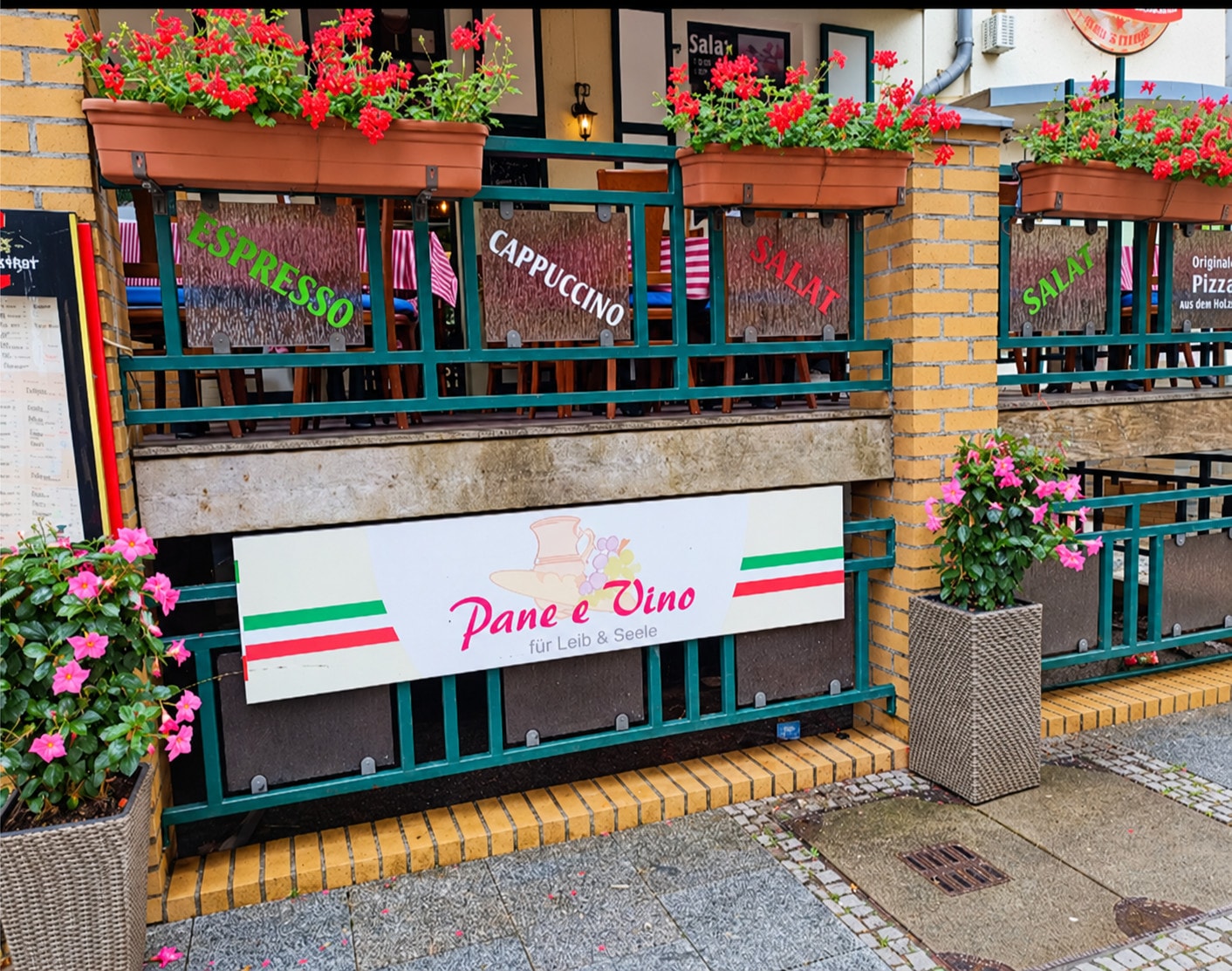The terrace railing with red geraniums and the “Pane e Vino – für Leib & Seele” sign