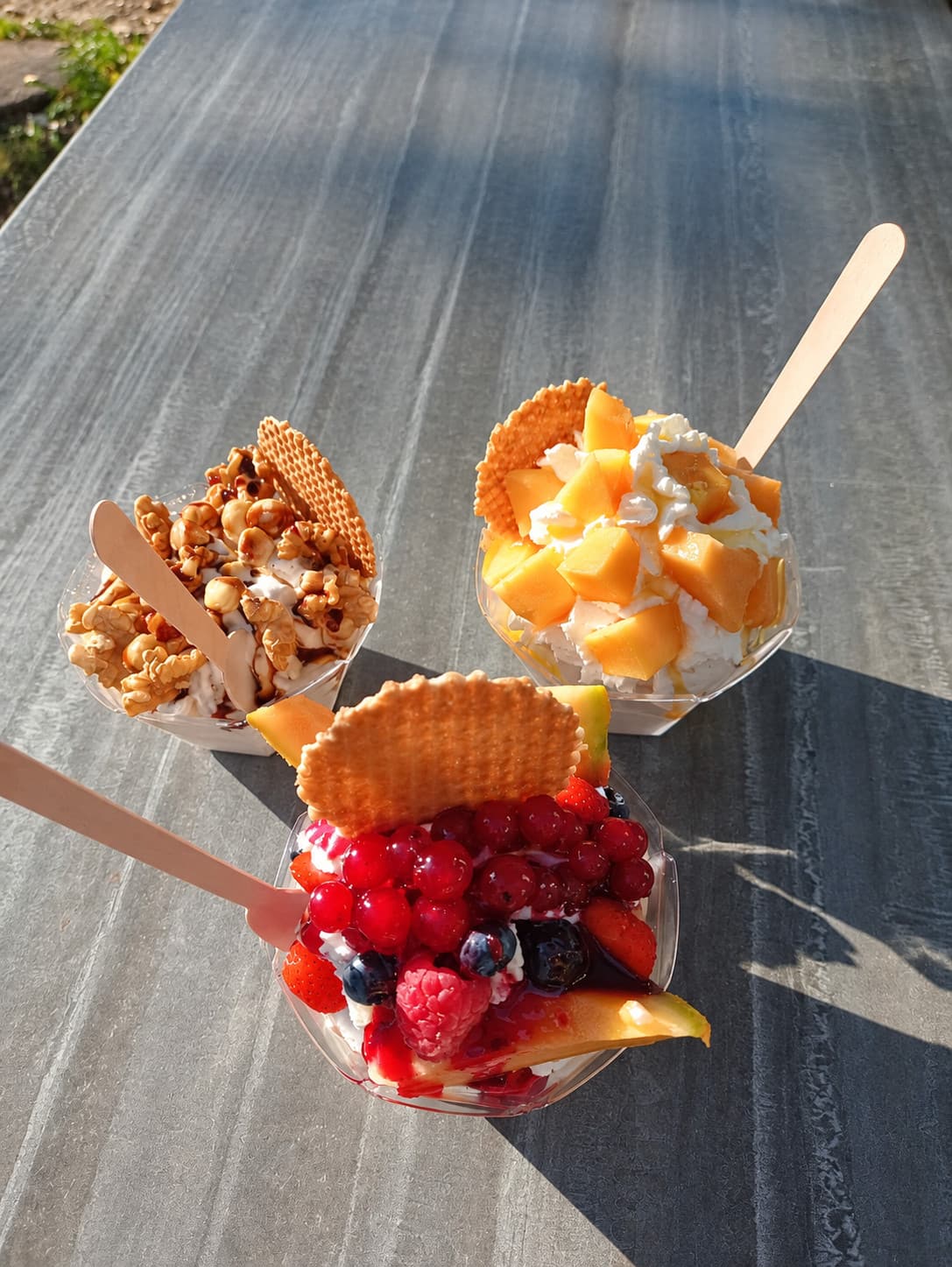 Three to-go cups with walnuts, mango and red berries, each with a wafer and a wooden spoon