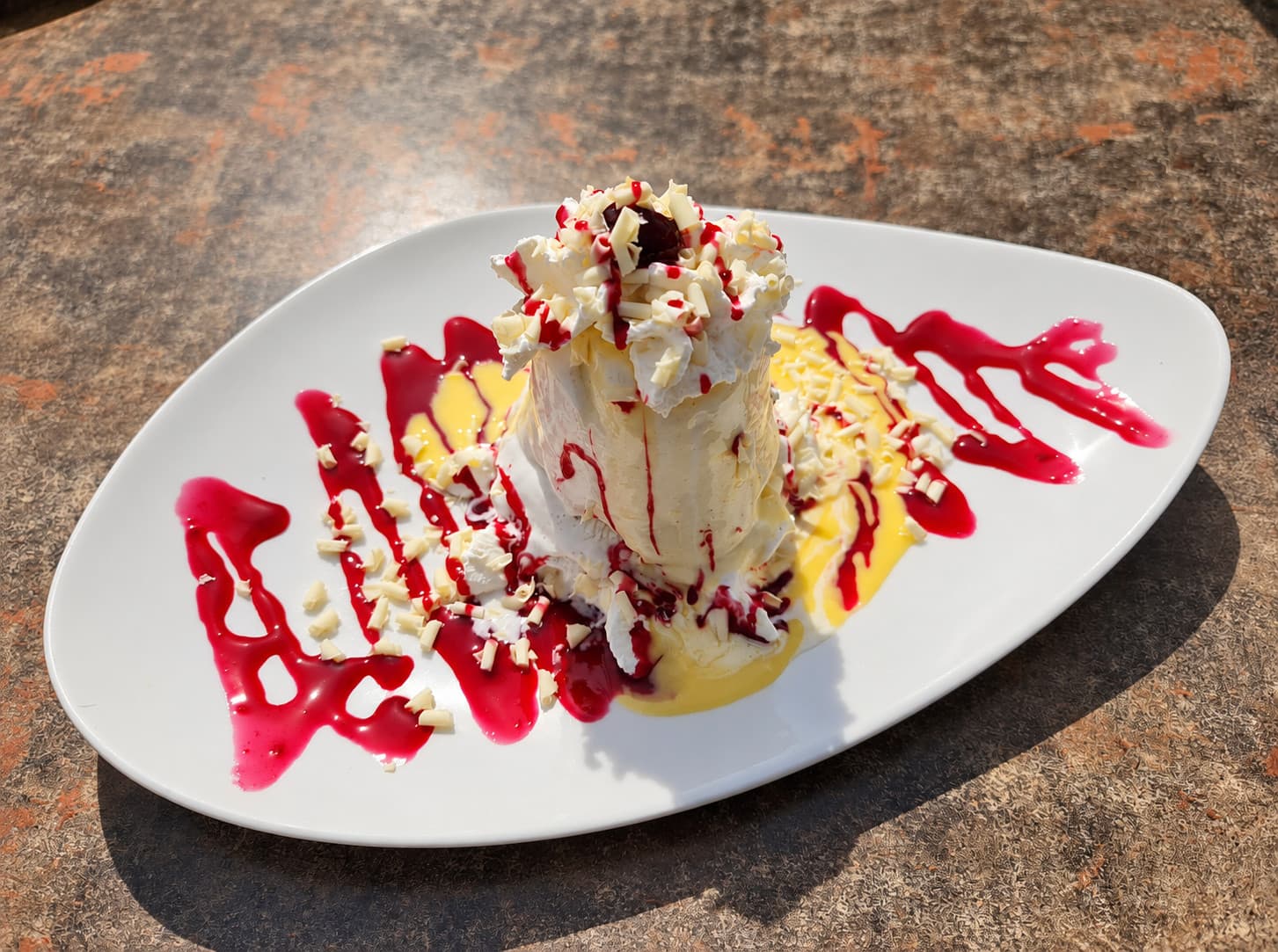 A tower of vanilla gelato with white chocolate curls, raspberry and vanilla sauce on an oval plate